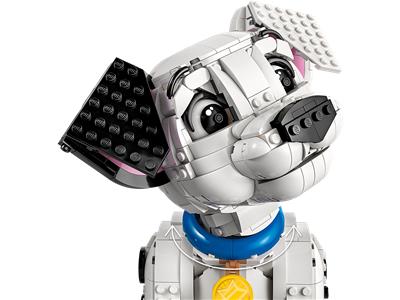 A close-up of a white and gray dog building block toy with black ears, a blue collar, and a yellow emblem on a white background.