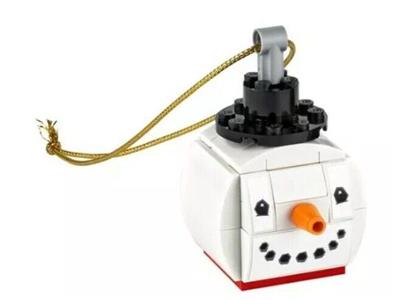 A LEGO snowman ornament made from white and black bricks, with a gold hanging string, an orange carrot nose, and a red base, shown on a plain white background.