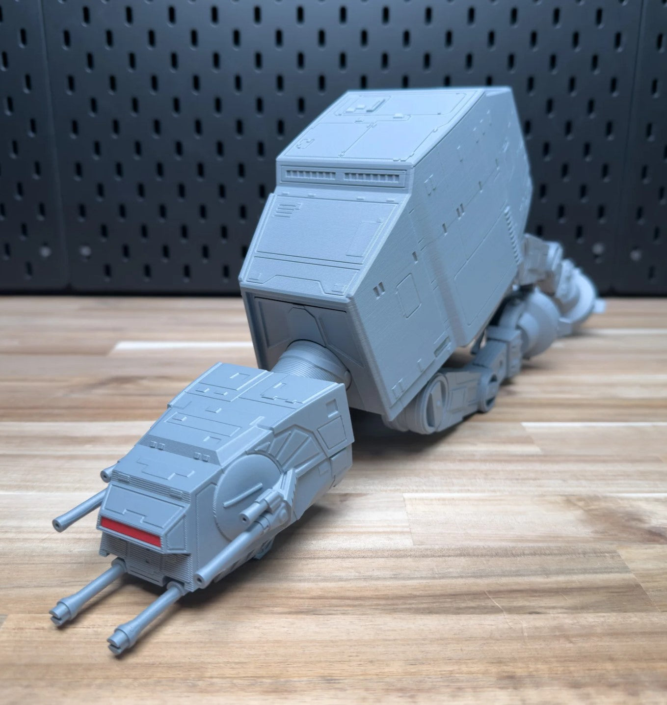 Toy model of a large vehicle or robot on a wooden surface with a perforated metal background.